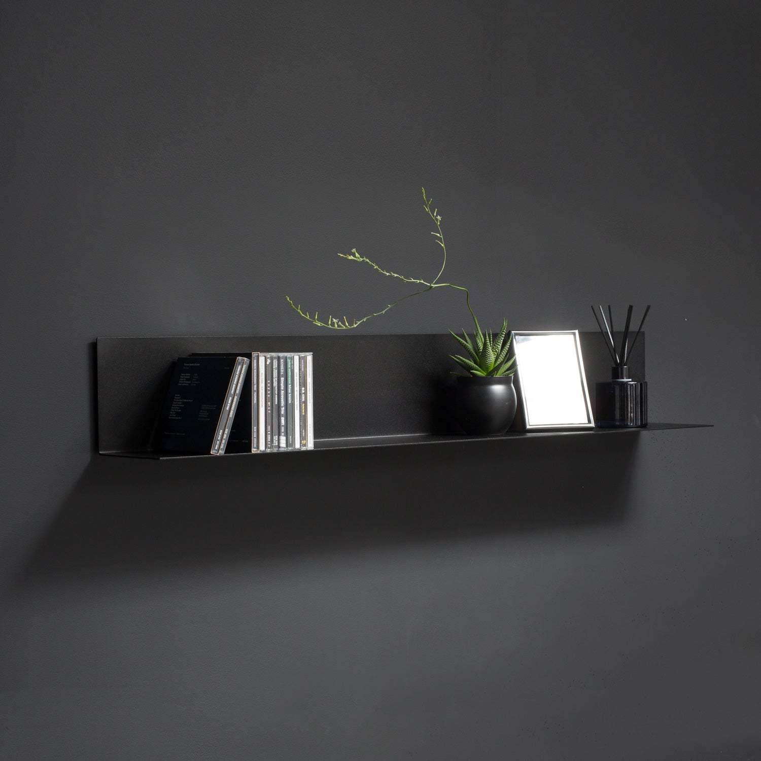 Black L shaped wall shelf hloding cd albums and decoration on black wall
