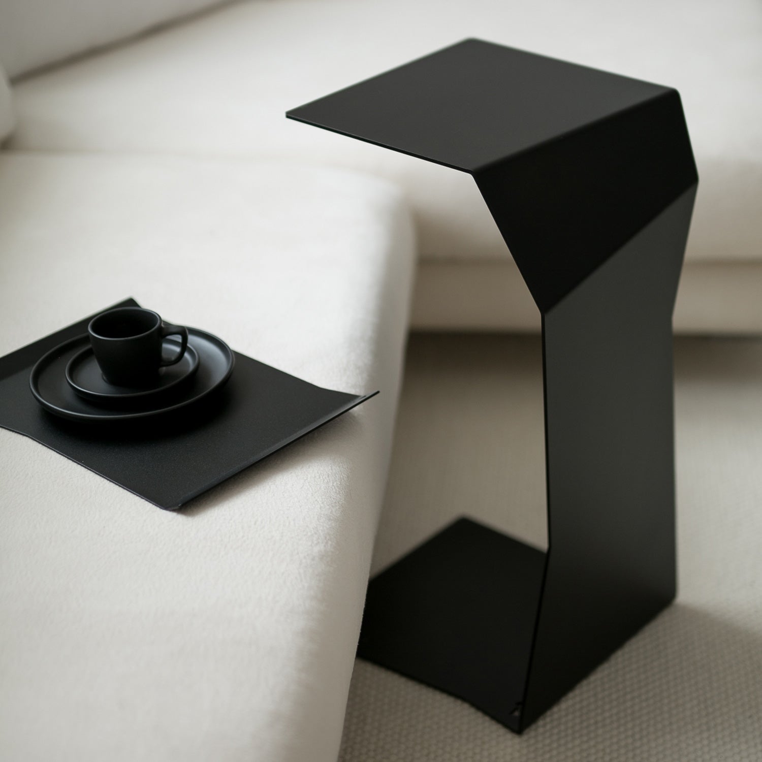 Modern black side table next to a white sofa with a black tray and cup.