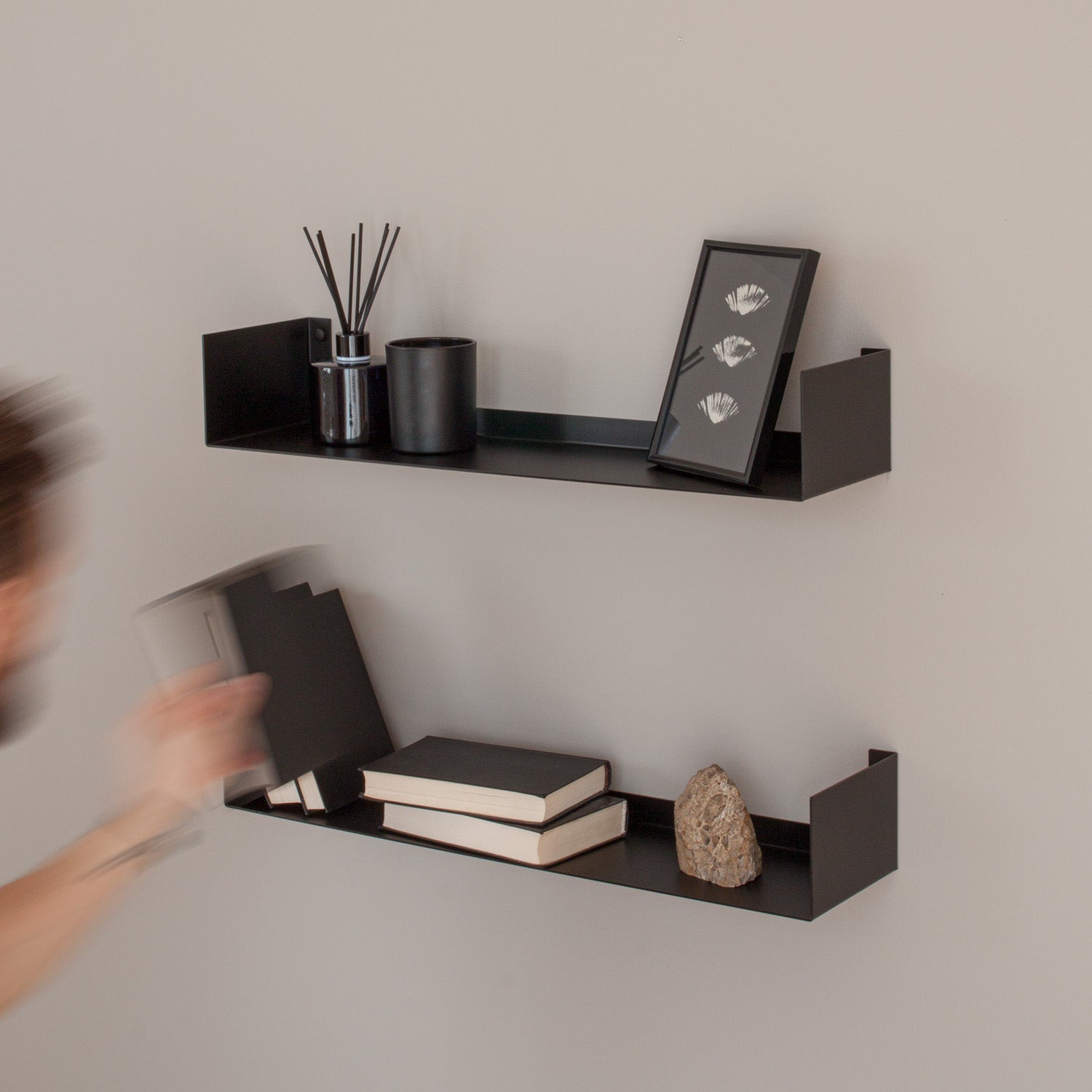 Black metal wall shelves with books, a stone, and decorative items against a plain wall.