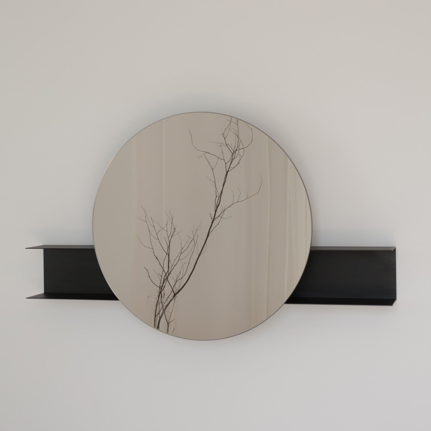 Round black wall mirror on a white wall with a black shelf.