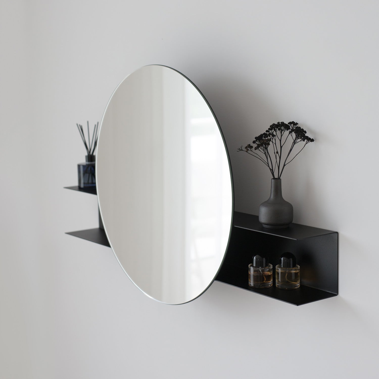 Black large round mirror with black shelf against a white wall with decorative items.