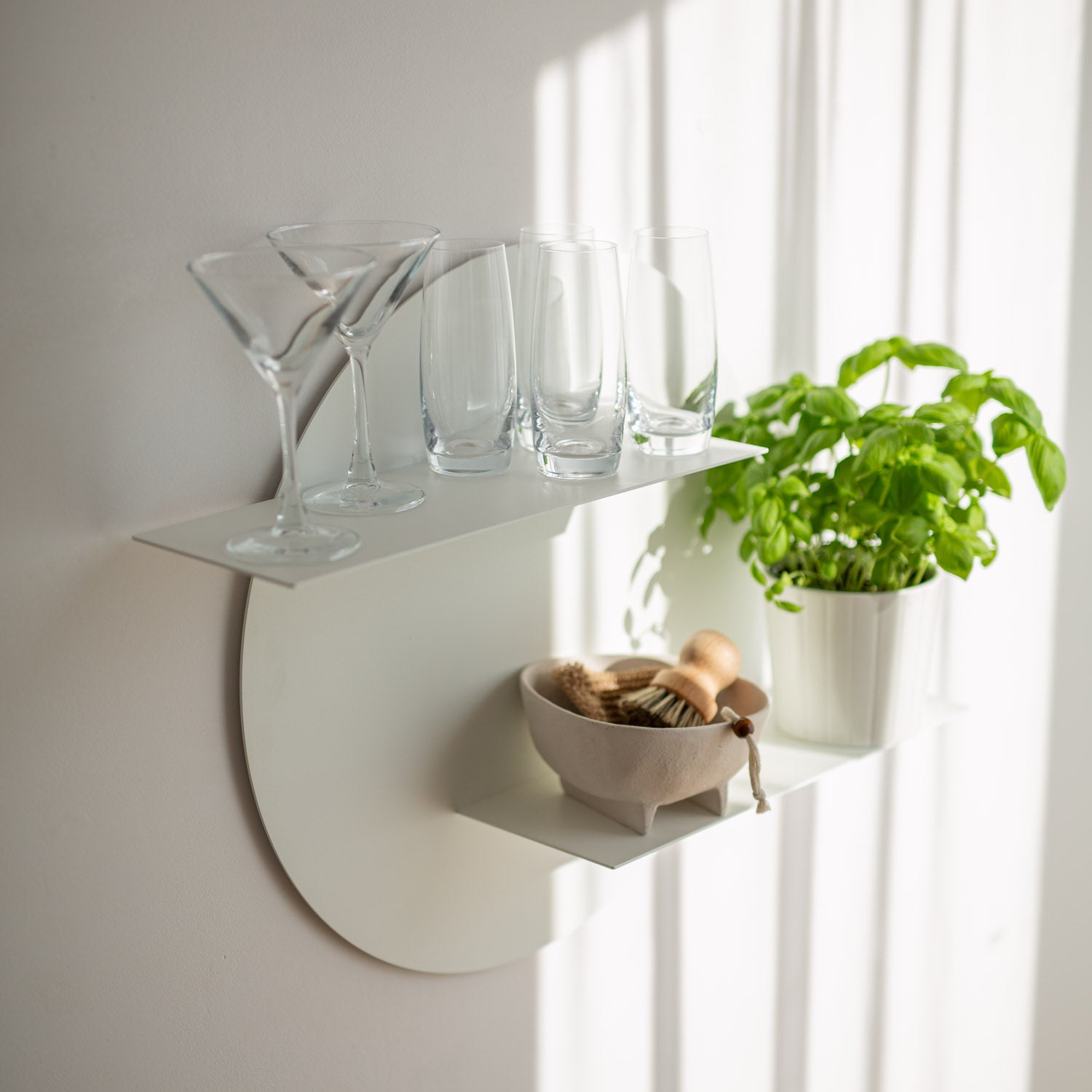 Wall-mounted round shelf with glasses, a bowl, and a plant against a white wall.