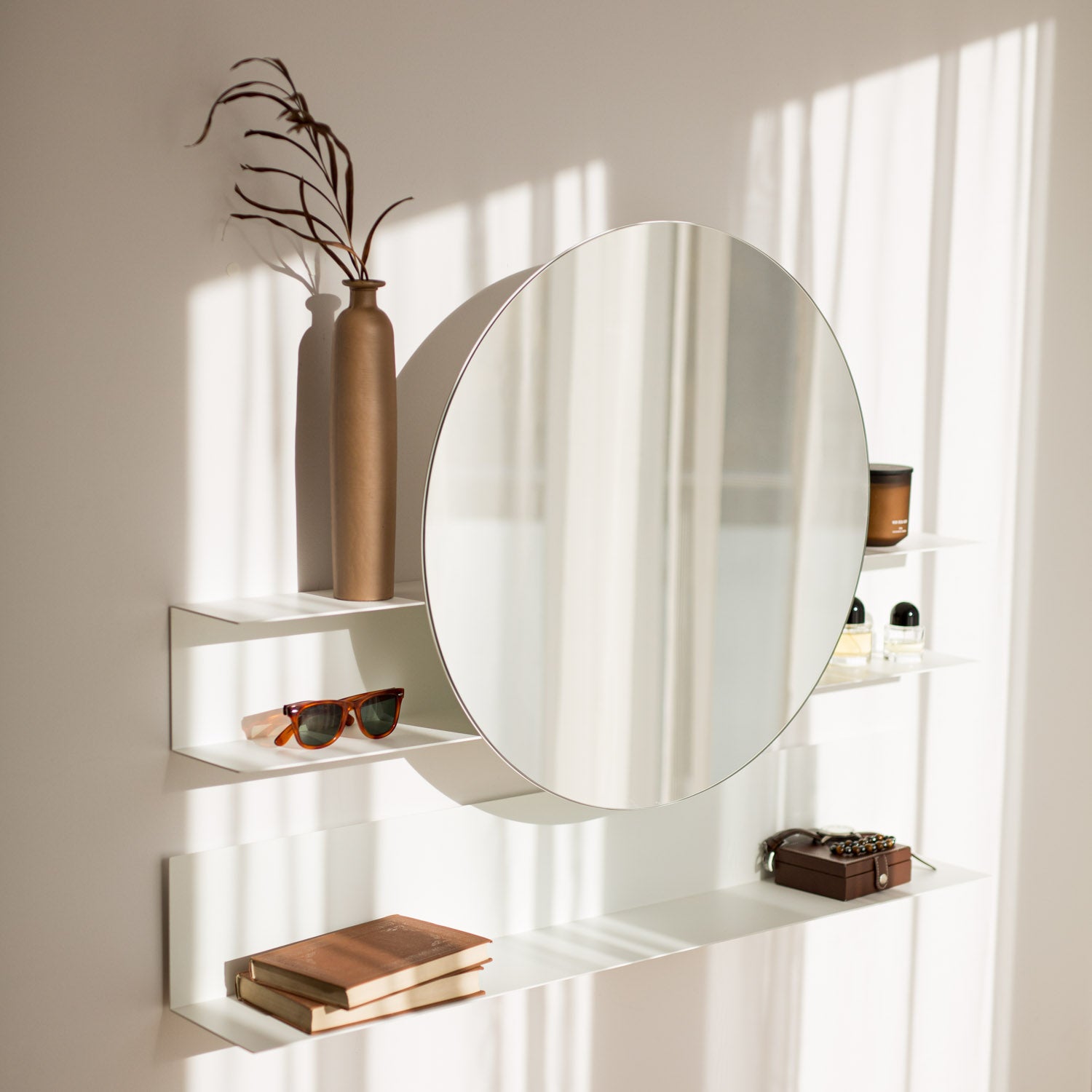 Round mirror on a wall with shelves holding decorative items.