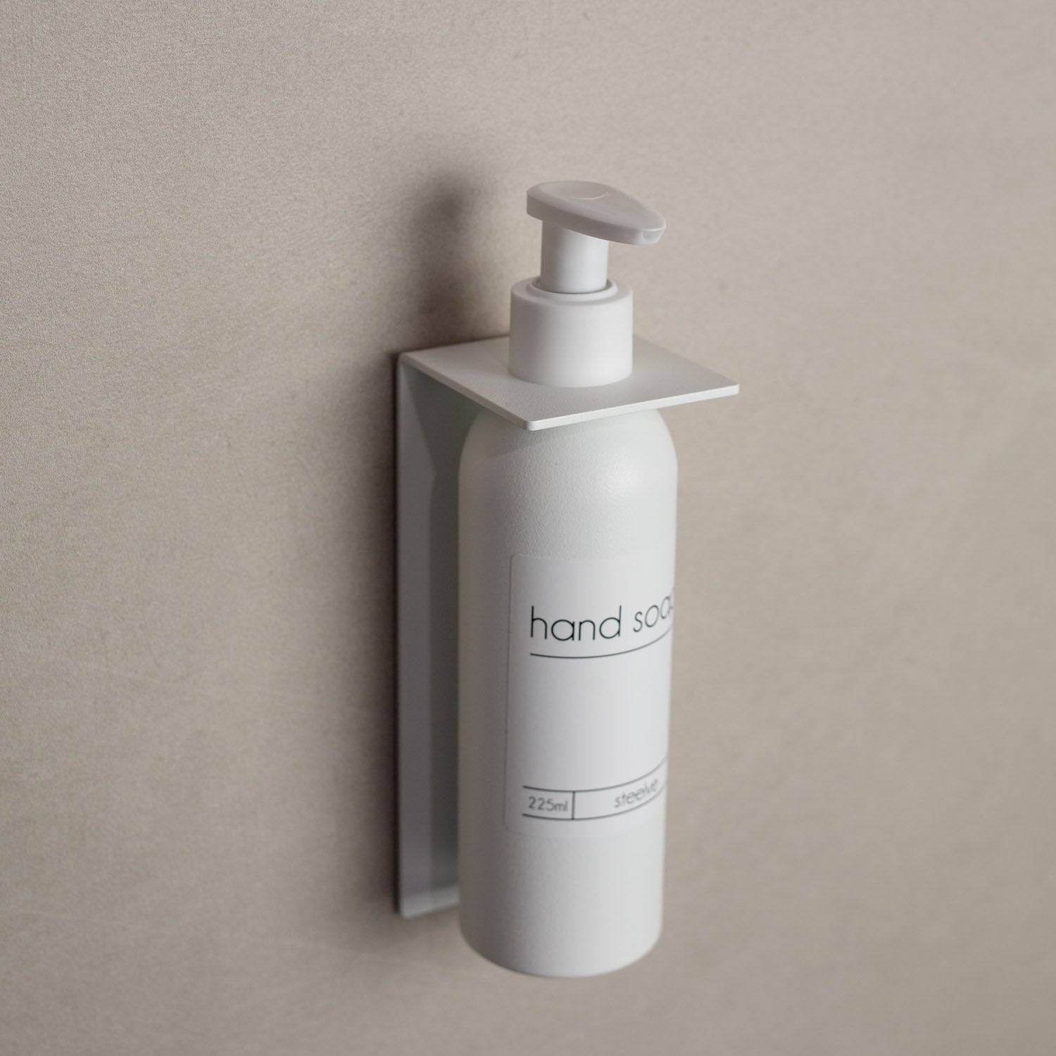 White hand soap dispenser mounted wihtout drilling on a beige wall
