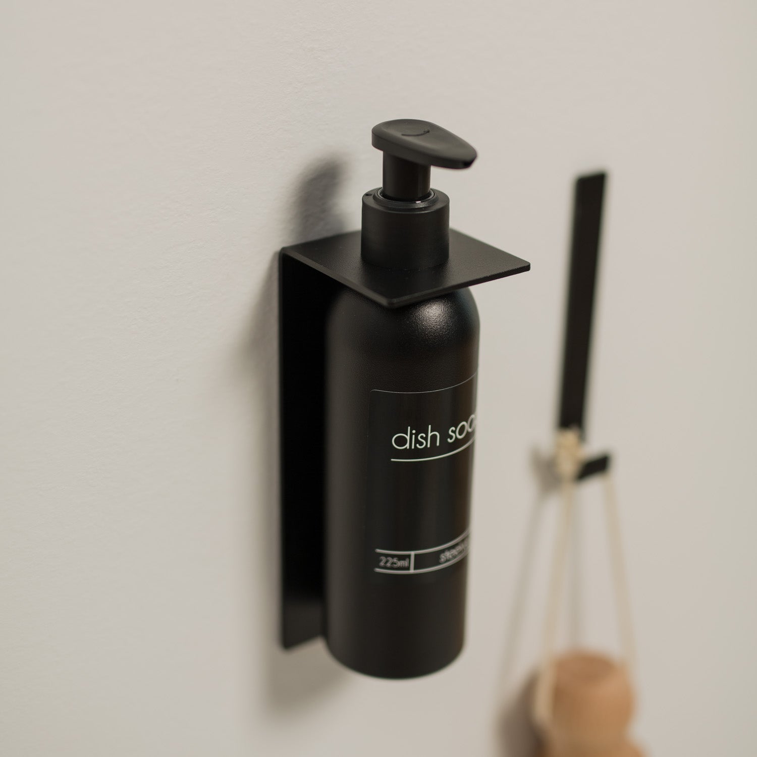 Black no-drill dish soap bottle with pump on a white wall