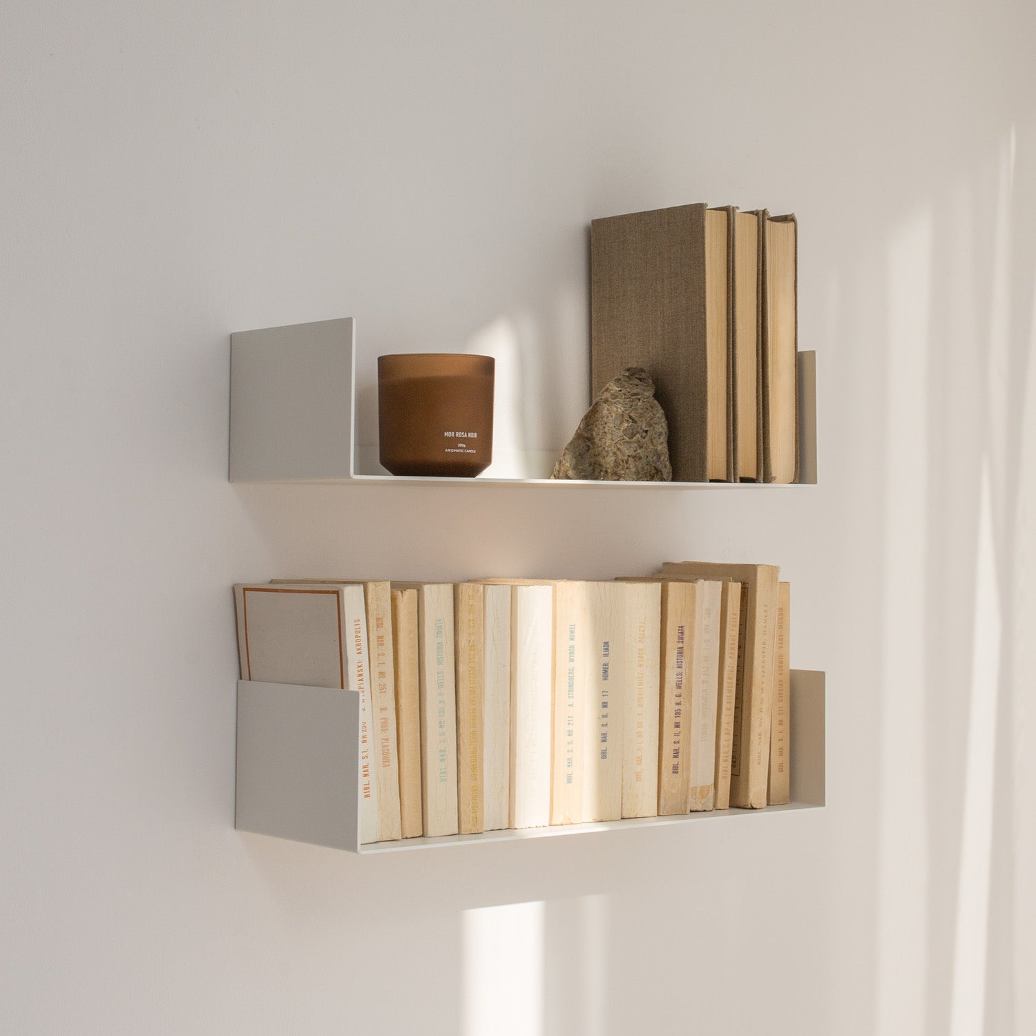 Wall-mounted shelves with books and a candle on a light gray background
