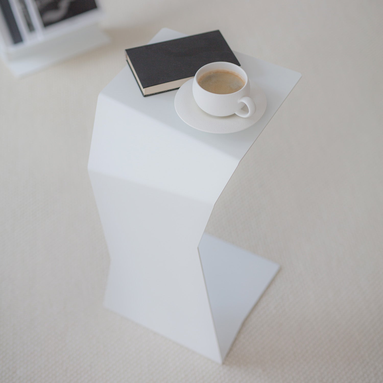 white modern side table with coffee cup and book on cream carpet