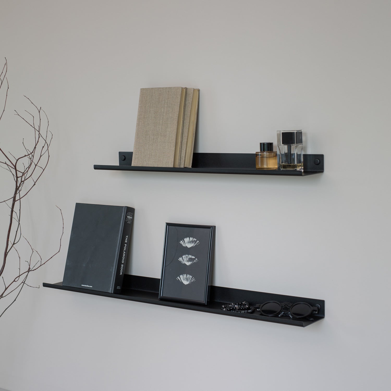 Black narrow wall shelves with books and decorative items against a white wall.
