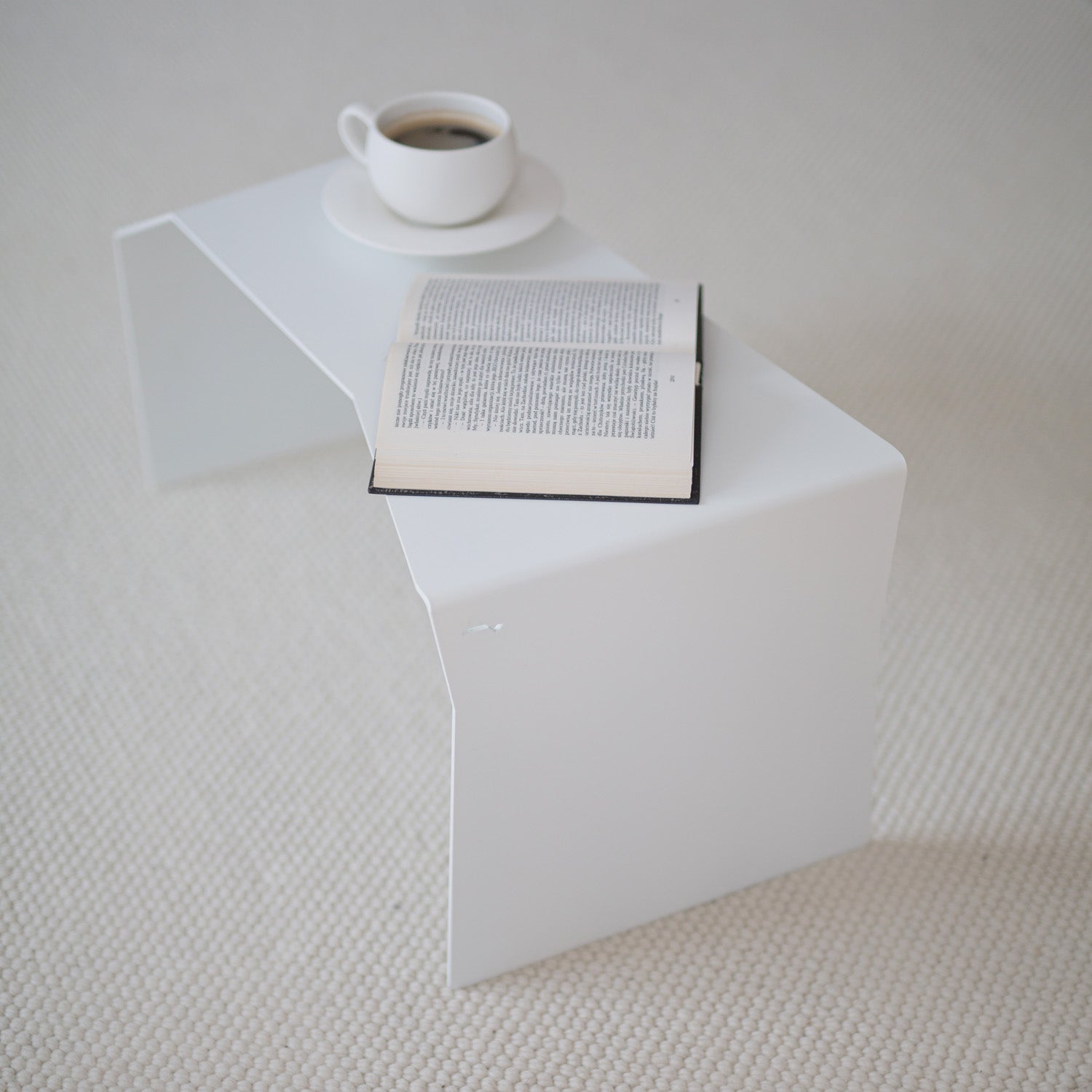 White modern coffee table with a book and a cup of coffee on a textured surface