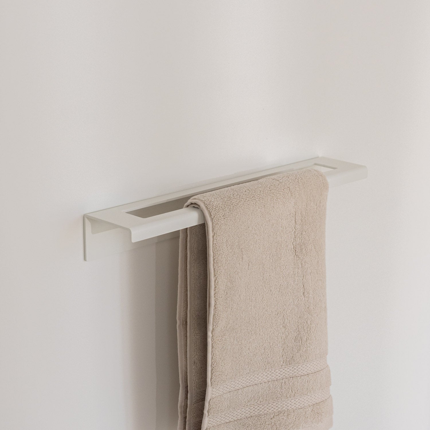 Beige towel hanging on a modern metal towel rack against a plain wall.