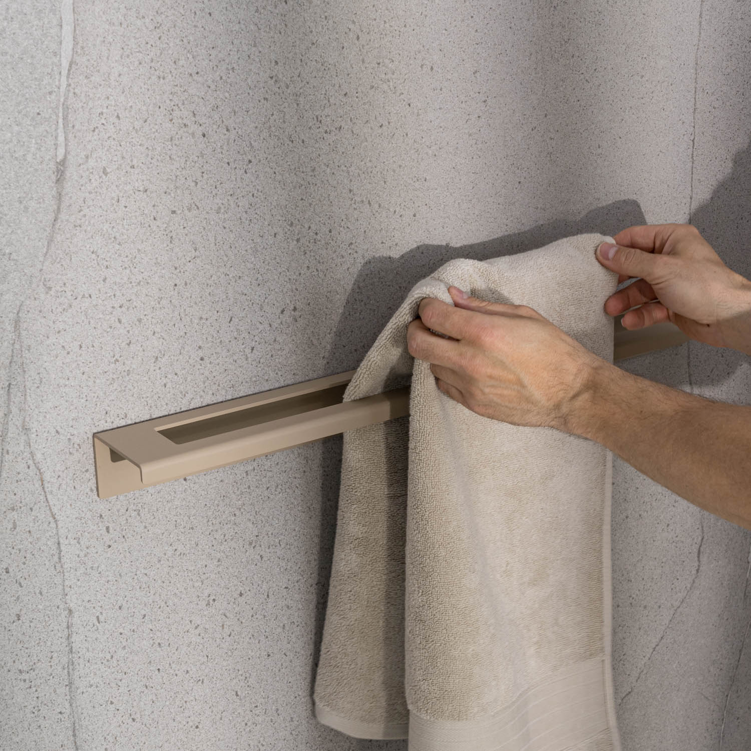 Person hanging a towel on a beige towel rack against a gray wall.
